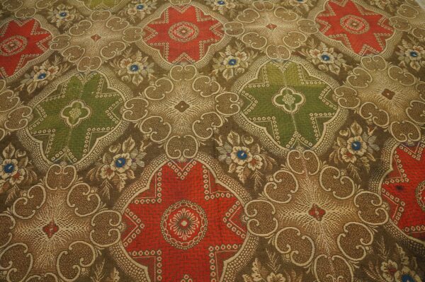 Ornate, low-pile rug detail showing alternating red and olive green medallions on a brown patterned field.