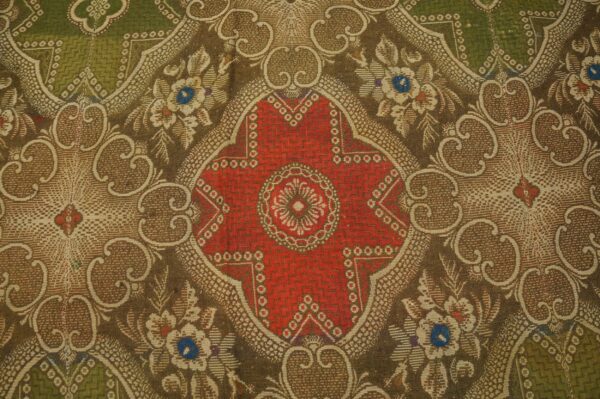 Close-up of an ornate, low-pile rug with a red medallion and floral scrolls in brown, olive green, and tan.