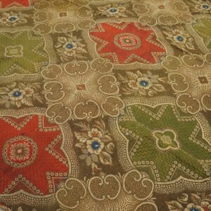 Woven rug with a complex pattern of red and green medallions on a brown scrollwork field.