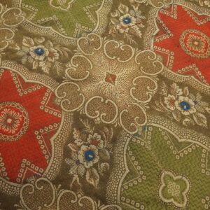 Detailed low-pile rug texture with repeating red and green medallions framed by tan and brown floral designs.