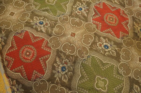 Detailed low-pile rug texture with repeating red and green medallions framed by tan and brown floral designs.