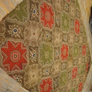 Brown, red, and olive green patterned textile featuring repeating star medallions on worn wood flooring.