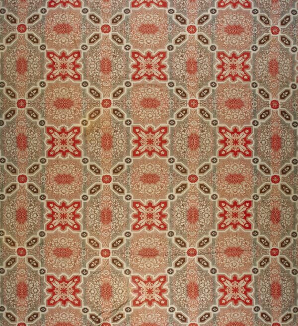 Low pile rug featuring repeating medallions and florals within a geometric lattice in red, taupe, and cream.