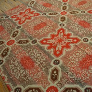 Red, cream, and brown rug featuring large geometric floral crosses covers worn wooden planks.