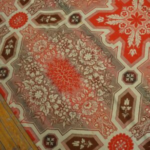 Detailed red and cream flatweave rug with large floral medallions and geometric borders on distressed wood floor.