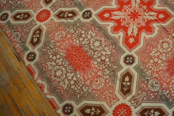Detailed red and cream flatweave rug with large floral medallions and geometric borders on distressed wood floor.