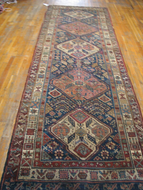 Runner rug with large geometric medallions in navy blue, rust, and tan on wood floors.