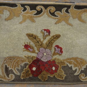 Textured brown and gold rug featuring an elaborate classical scrolling border and central red flowers on light wooden flooring.