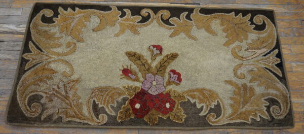 Textured brown and gold rug featuring an elaborate classical scrolling border and central red flowers on light wooden flooring.