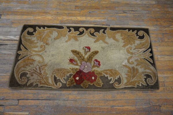 Low-pile beige rug with dark brown border, golden scrollwork, and central red and purple floral bouquet on wood flooring.