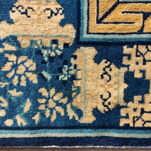 High-pile rug featuring bold blue and tan interlocking geometric and floral border designs.