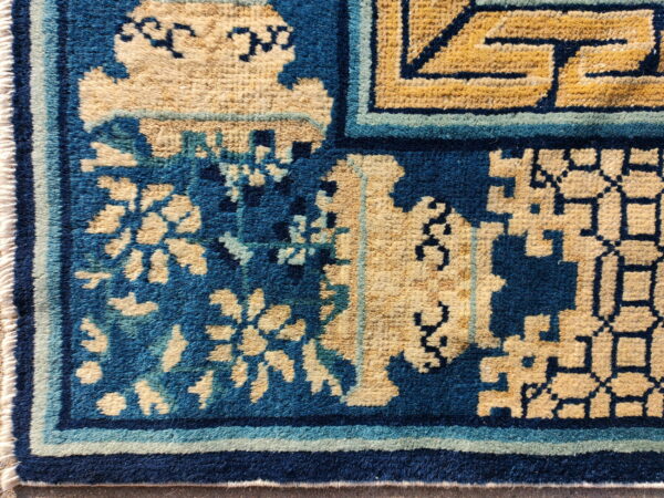 High-pile rug featuring bold blue and tan interlocking geometric and floral border designs.