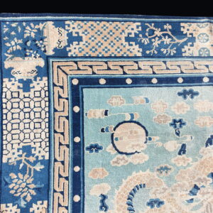 Corner detail of a light and dark blue rug with complex geometric borders and stylized cloud motifs in the field.