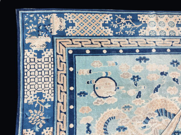 Corner detail of a light and dark blue rug with complex geometric borders and stylized cloud motifs in the field.