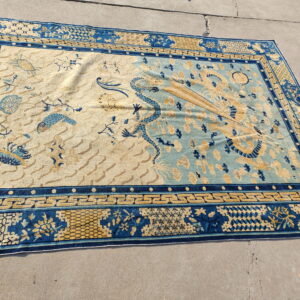 Blue and beige rug with a split field, central dragon, and geometric borders lies on concrete pavement.