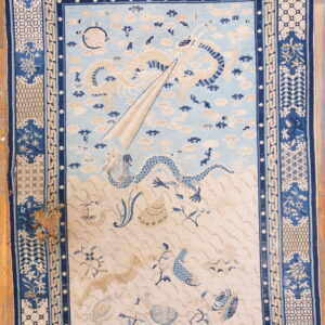Pale blue and cream rug with detailed dragon and sea life pattern on wooden floorboards.