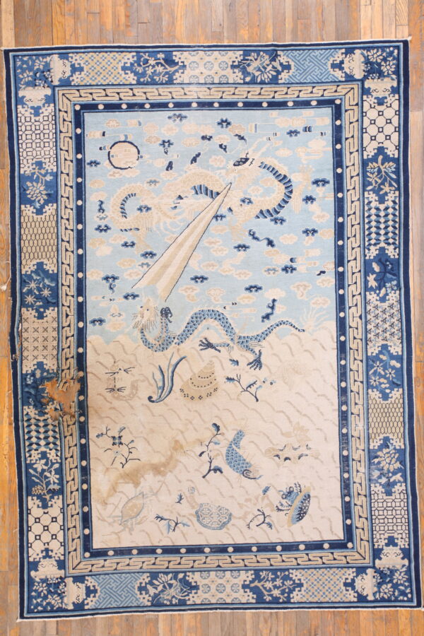 Pale blue and cream rug with detailed dragon and sea life pattern on wooden floorboards.