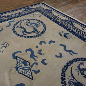 Blue dragon and symbolic motifs on a beige rug field laid upon worn wood flooring.