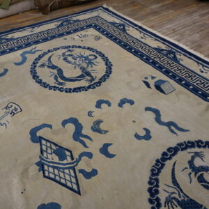 Blue and cream rug featuring a dragon pattern, key border, and visible fringe on worn wood planks.