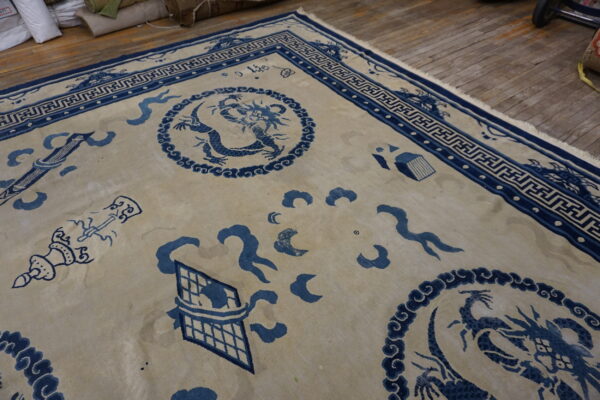 Blue and cream rug featuring a dragon pattern, key border, and visible fringe on worn wood planks.