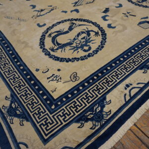 Beige and blue rug with dragon motifs and meander borders displayed over distressed wooden floorboards.