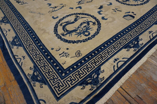 Beige and blue rug with dragon motifs and meander borders displayed over distressed wooden floorboards.