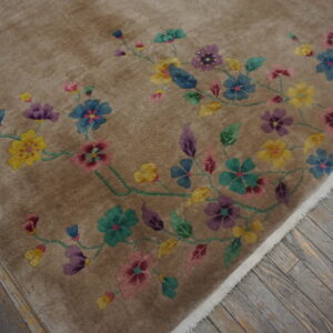 High-pile taupe rug with a winding multi-colored floral design rests on distressed gray wood flooring.