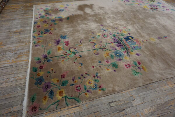 A lush tan rug displaying a bright, multicolored floral and vine design over gray wooden flooring.