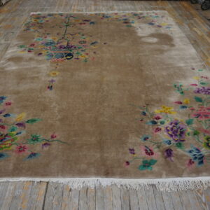 A large, tan rug with bright multicolored floral motifs, including a vase centerpiece, rests on distressed wood planks.