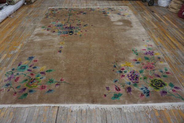 A large, tan rug with bright multicolored floral motifs, including a vase centerpiece, rests on distressed wood planks.