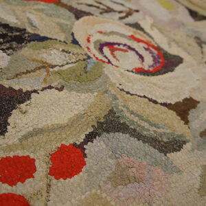 Textured, high-pile rug close-up featuring floral and berry shapes in beige, green, brown, and red.