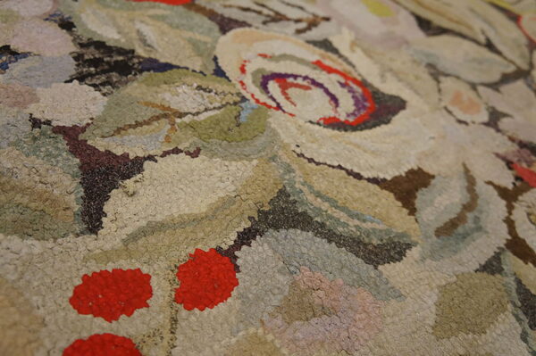 Textured, high-pile rug close-up featuring floral and berry shapes in beige, green, brown, and red.