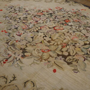 Muted floral rug with a central spray of red and pale flowers against a textured light tan background.