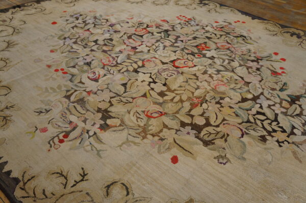 Muted floral rug with a central spray of red and pale flowers against a textured light tan background.