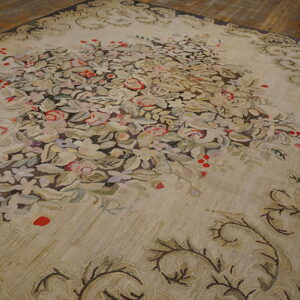 Large beige rug with a lush central floral bouquet and scrolling border resting on hardwood floor planks.