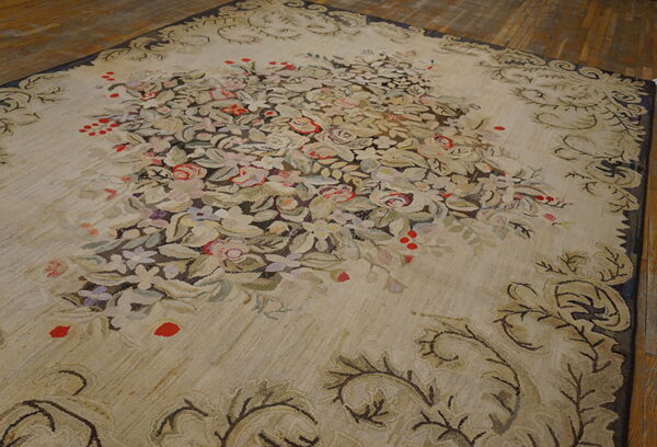 Large beige rug with a lush central floral bouquet and scrolling border resting on hardwood floor planks.