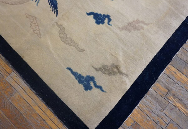 Light beige low-pile rug with blue, brown, and pink abstract patterns, bordered in dark navy on wood flooring.