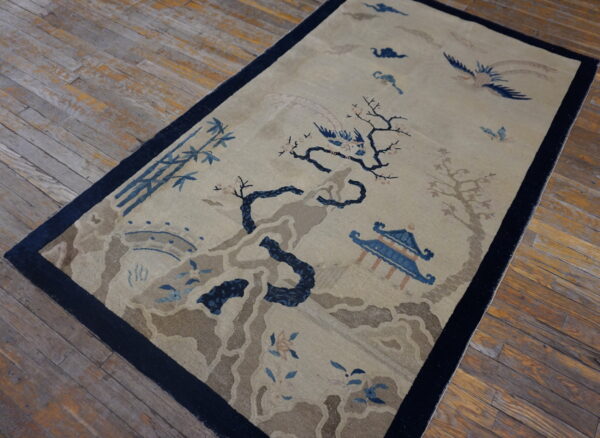 Beige rug with navy border and blue scenic pattern of trees, birds, and a pavilion on rustic wood floors.