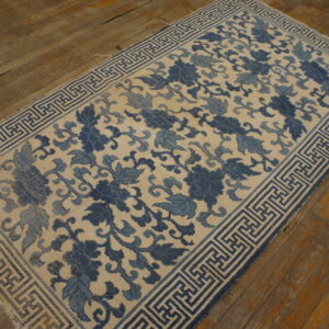 Cream and dual-toned blue floral rug with a geometric border rests on brown wood planks.