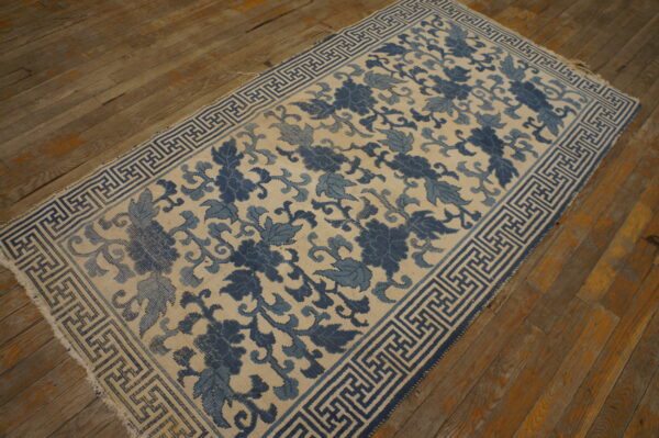 Cream and dual-toned blue floral rug with a geometric border rests on brown wood planks.