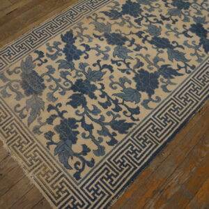 Cream rug with indigo floral pattern and blue geometric key border on distressed wood floor.
