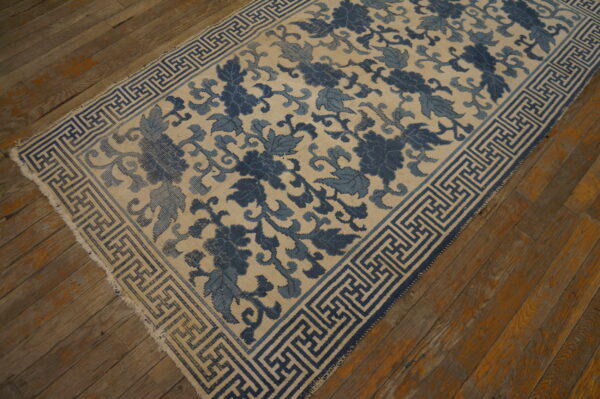 Cream rug with indigo floral pattern and blue geometric key border on distressed wood floor.