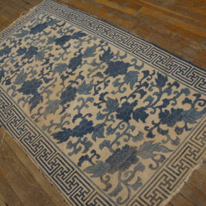 Cream and blue rug with large stylized florals and a meander border on distressed wood flooring.