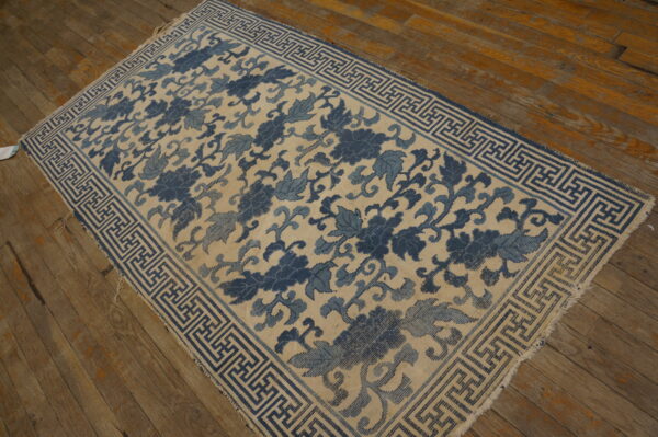 Cream and blue rug with large stylized florals and a meander border on distressed wood flooring.