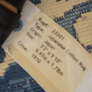 Blue and cream patterned rug with a textured pile is partially covered by a product tag listing it as Japanese Cotton Rug.