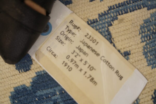 Blue and cream patterned rug with a textured pile is partially covered by a product tag listing it as japanese cotton rug.