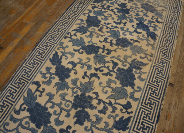 Low-pile runner featuring blue floral motifs and a key pattern border rests on rustic wood planks.