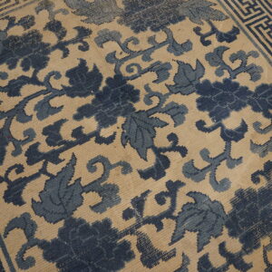 Beige rug featuring dark blue botanical patterns and a detailed geometric key border.