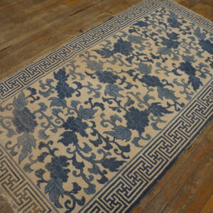 Indigo and cream rug with a continuous floral design and geometric border on distressed wood flooring.