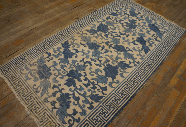 Indigo and cream rug with a continuous floral design and geometric border on distressed wood flooring.